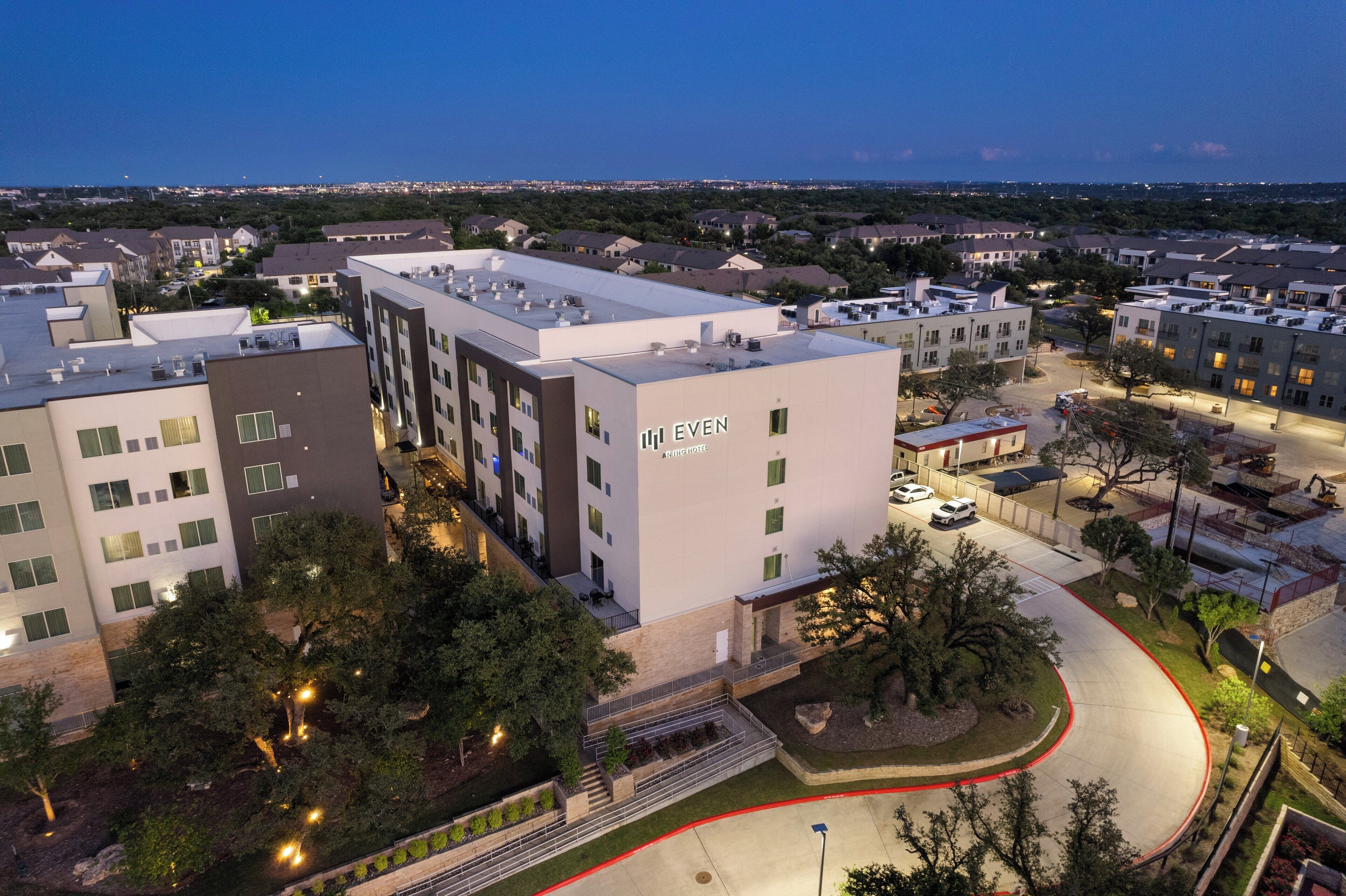 A multi-story hotel with a flat roof, a landscaped courtyard, and a parking area.