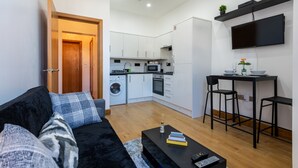 A compact living space with a kitchenette, a sofa, a coffee table, and a TV mounted on the wall.