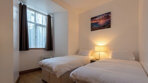 A bedroom with two beds, a window with curtains, a radiator, and a painting on the wall.