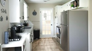 A compact kitchen with white cabinets, a stainless steel refrigerator, a coffee maker, and a trash bin. - The Cozy Corner, Family Friendly, Game Room + WiFi (Woodward)
