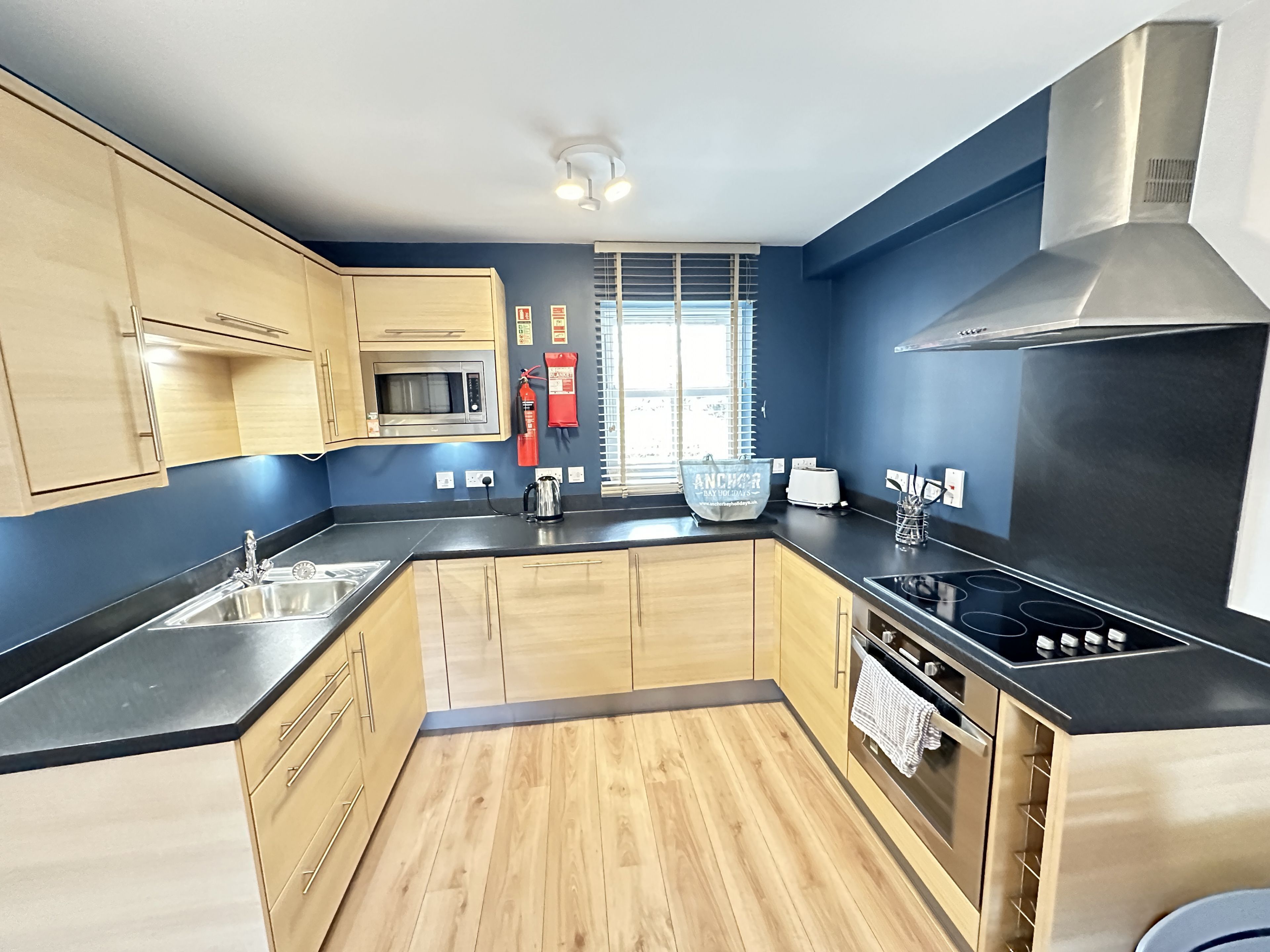 A modern kitchen with wooden cabinets, a stainless steel sink, a microwave, a gas stove, and a large window with blinds.