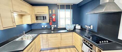 A modern kitchen with wooden cabinets, a stainless steel sink, a microwave, a gas stove, and a large window with blinds.