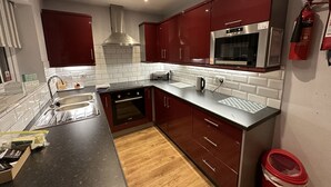 Een moderne keuken met roestvrijstalen apparatuur, rode keukenkastjes en een betegelde achterwand met ruitpatroon.