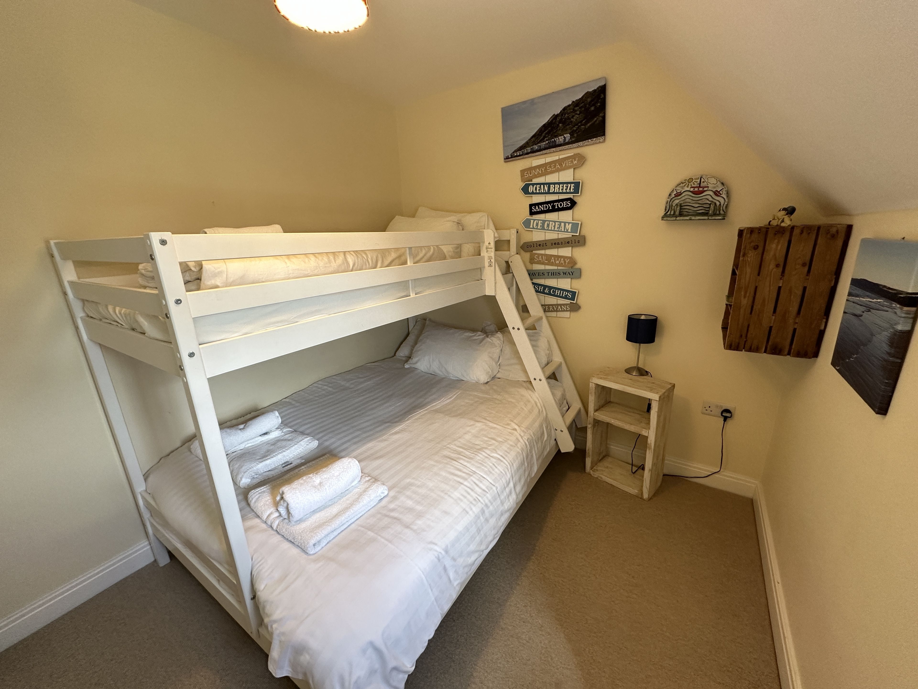 Een slaapkamer met stapelbed, een klein nachtkastje, een lamp en een muur met nautische decoraties.