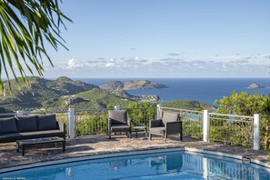 Zona junto a la piscina con vista al océano y las colinas.