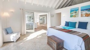 Une chambre avec un grand lit, une commode en bois, un canapé agrémenté d’un coussin à motifs et une vue sur un balcon.