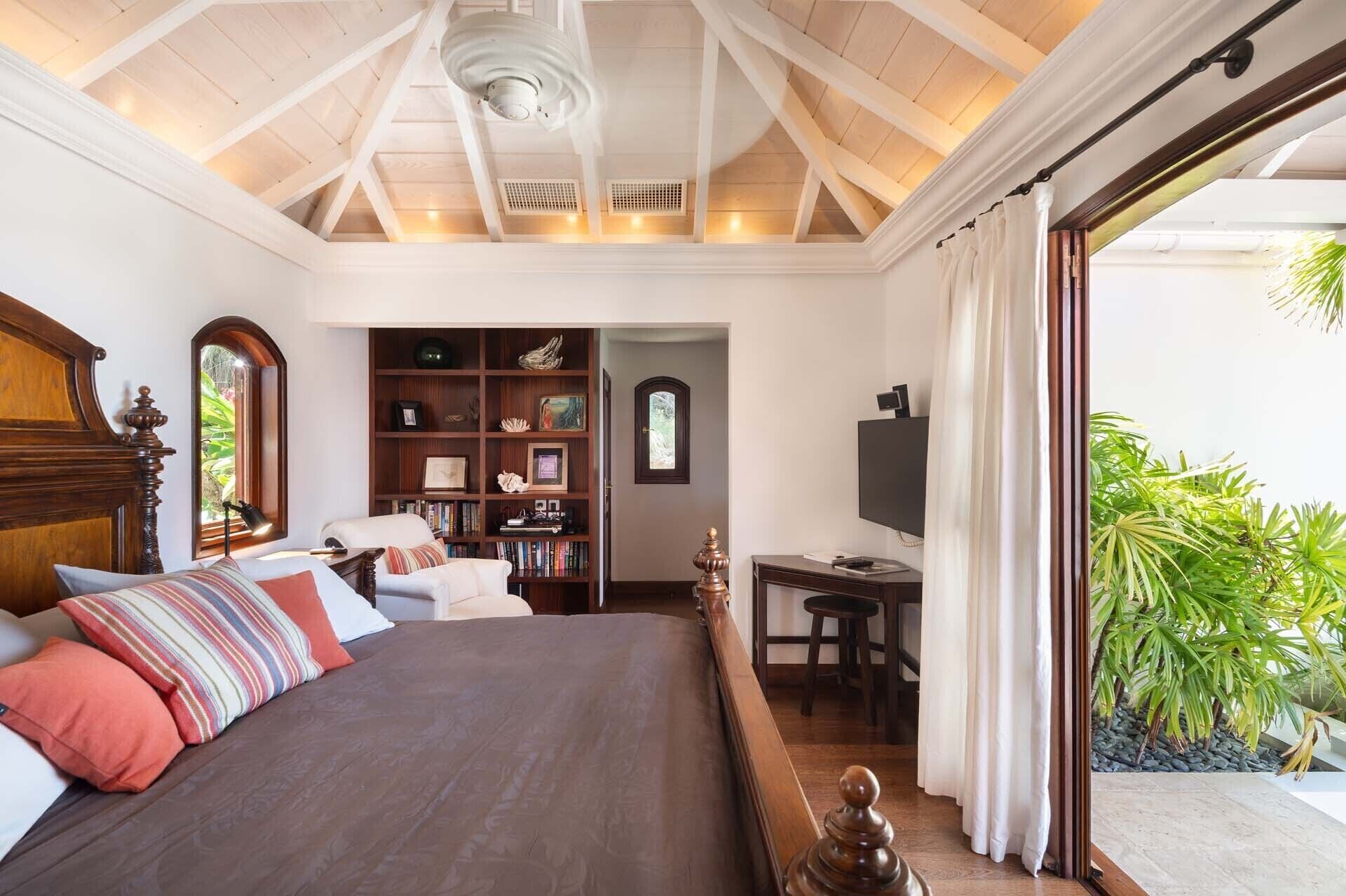 A bedroom with a large bed, a wooden headboard, a bookshelf, a desk, and a television.
