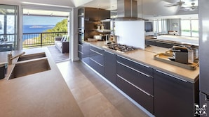A modern kitchen with a large island, stainless steel appliances, and a view of the ocean.