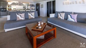 A modern living room with two grey sofas, a wooden coffee table, and a kitchen in the background.