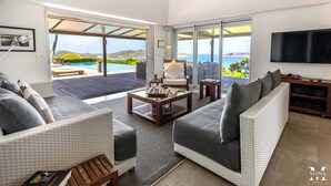 A spacious living room with a large TV, comfortable seating, and a view of a pool and ocean.