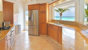 Una cocina con armarios de madera, un refrigerador de acero inoxidable, un horno empotrado y un ventanal con vistas a la playa.