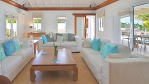 Un salón luminoso con dos sofás blancos, una mesa de centro de madera y vistas a un patio exterior.