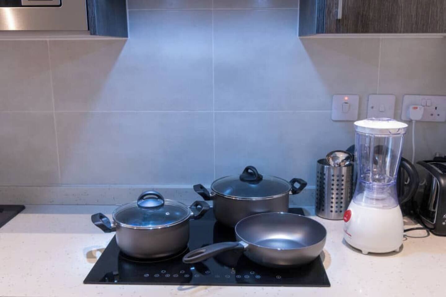 Een keuken met een fornuis, pannen, een blender en een waterkoker.