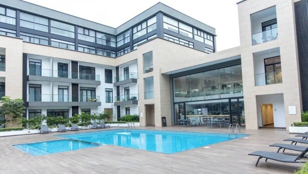 A modern building with a swimming pool, lounge chairs, and a restaurant area. - Plush Studio @Embassy Gardens (Accra)