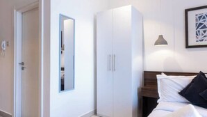 A bedroom with a bed, a wardrobe, a mirror, and a wall-mounted light fixture. - Plush Studio @Embassy Gardens (Accra)