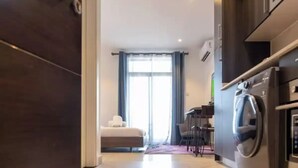 A modern hotel room with a large bed, a dining area, and a kitchen with a built-in oven and microwave. - Plush Studio @Embassy Gardens (Accra)