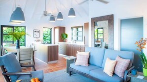 Ein modernes Wohnzimmer mit einem blauen Sofa, einem Esstisch und einer Küchenzeile mit Holzschränken und einem großen Fenster.