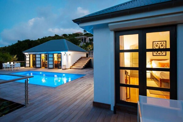 A modern house with a swimming pool, wooden deck, and a well-lit interior.