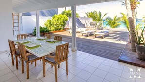 Comedor moderno con mesa de vidrio y sillas de madera, con vista a una piscina y palmeras.
