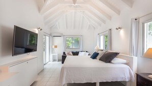 Ein Schlafzimmer mit einem großen Bett, einem an der Wand befestigten Fernseher und einem Fenster, das für natürliches Licht sorgt.