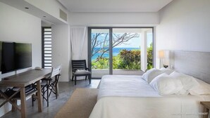 Una habitación de hotel moderna con una cama grande, un escritorio con silla, televisor y un balcón con vistas al océano.
