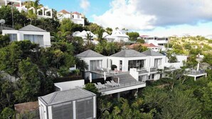 Una propiedad en la ladera con edificios blancos modernos, incluyendo una casa grande con balcón y una construcción más pequeña con techo de metal.