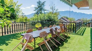 Een buiten eethoek met een tafel en stoelen, omringd door een houten hek, en een uitzicht op bergen in de verte.