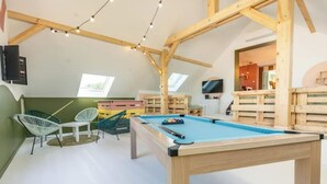 Een zolderkamer met een pooltafel, stoelen en houten balken.