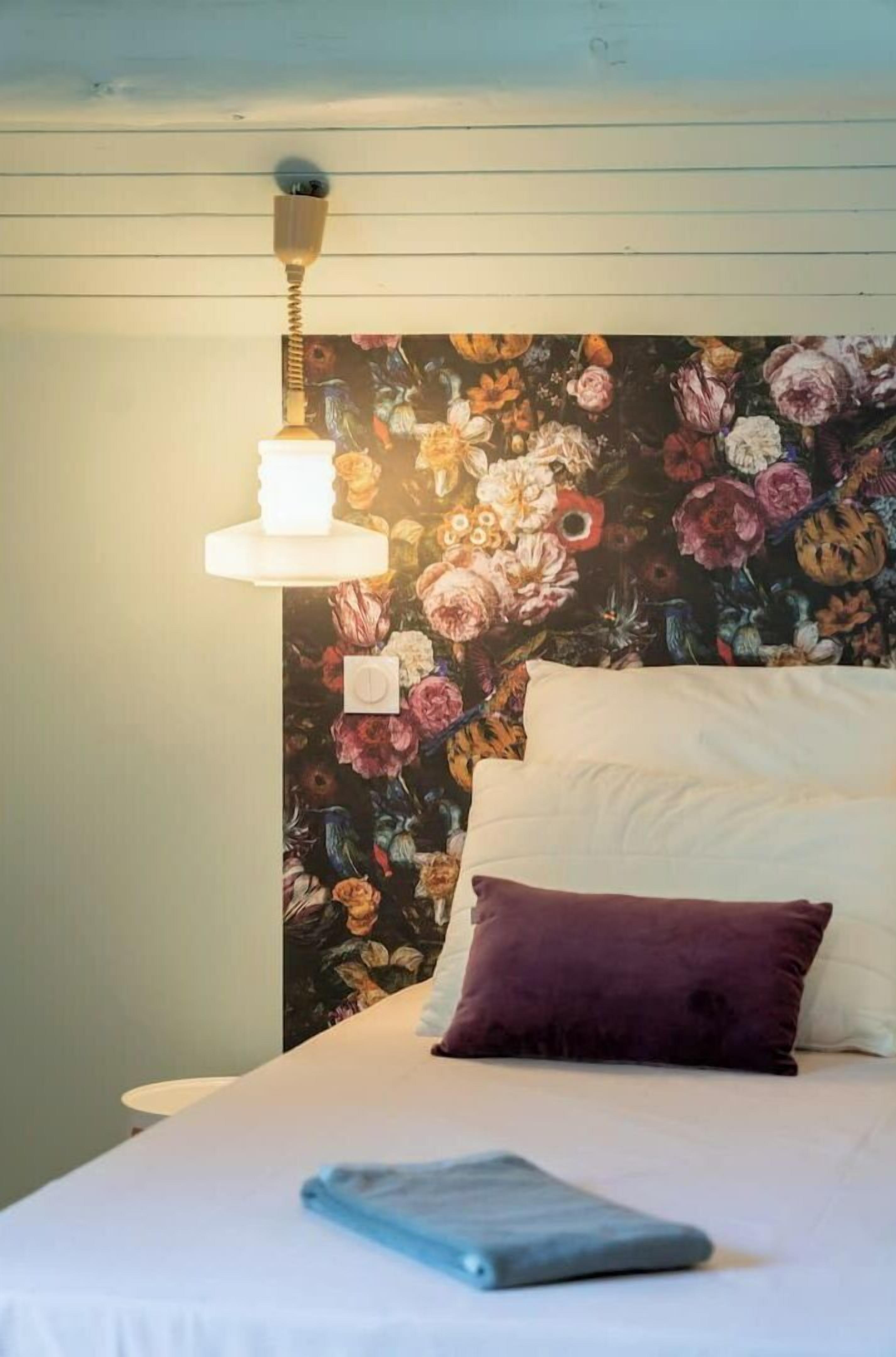 Een bed met een bloemen hoofdbord, een wit kussen, een paars kussen en een blauwe deken.