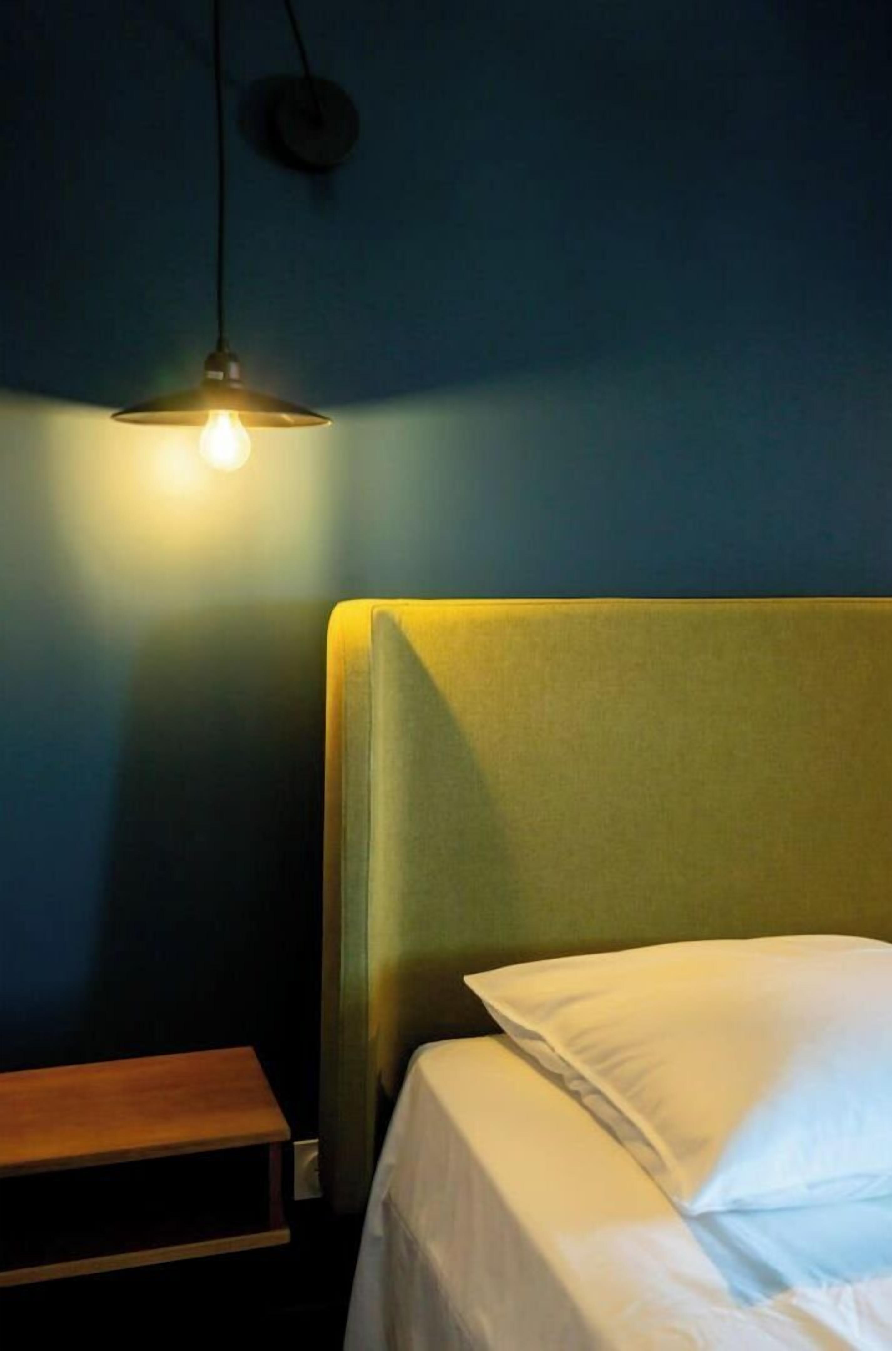 A bedroom with a single bed, a bedside table, and a hanging light fixture.