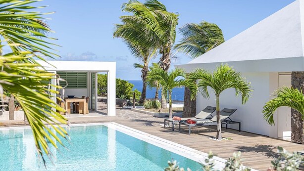 Un área de piscina moderna con vista despejada al mar, una terraza de madera y sillones de descanso.
