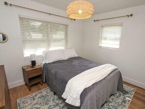 A bedroom with a bed, nightstand, bedside lamp, and a hanging light fixture. - Charming and cozy cottage in Davidson, NC (Davidson)