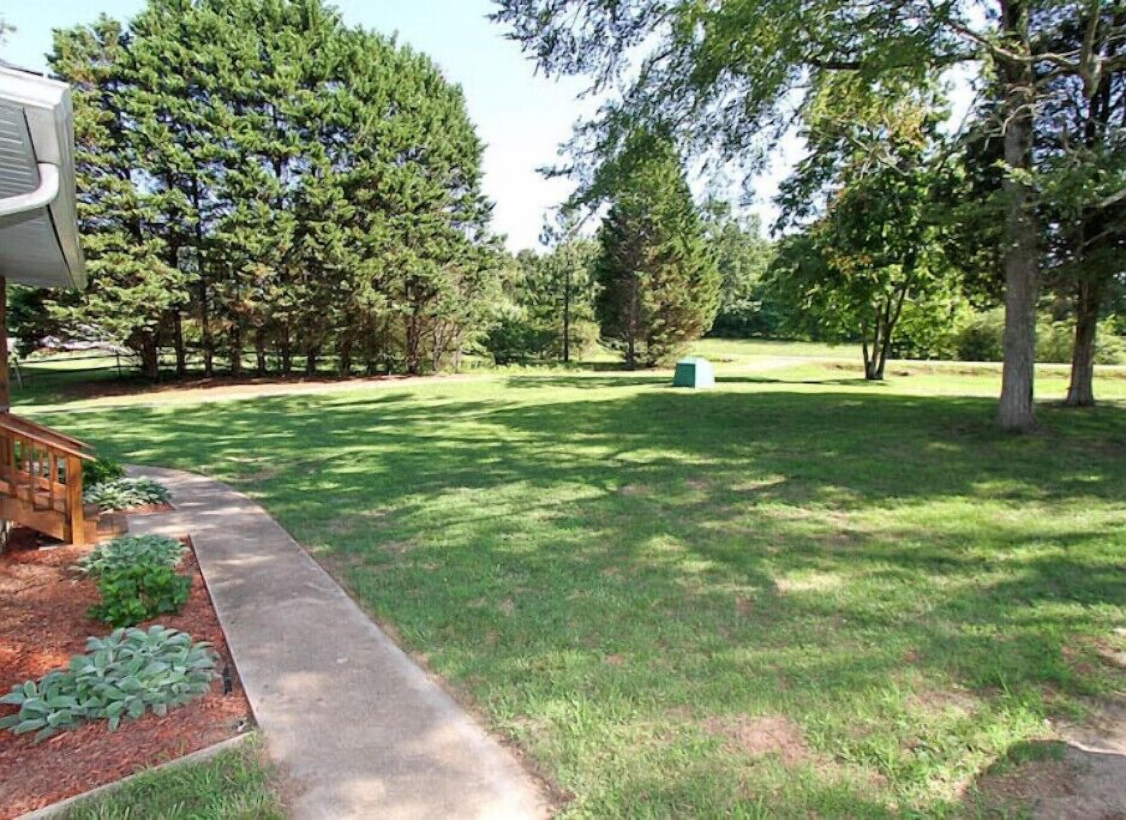 A well-maintained grassy yard with a concrete path leading to a wooden deck.