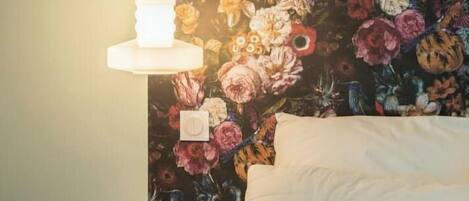 Un lit avec une tête de lit à motifs floraux, un oreiller blanc, un oreiller violet et une couverture bleue.