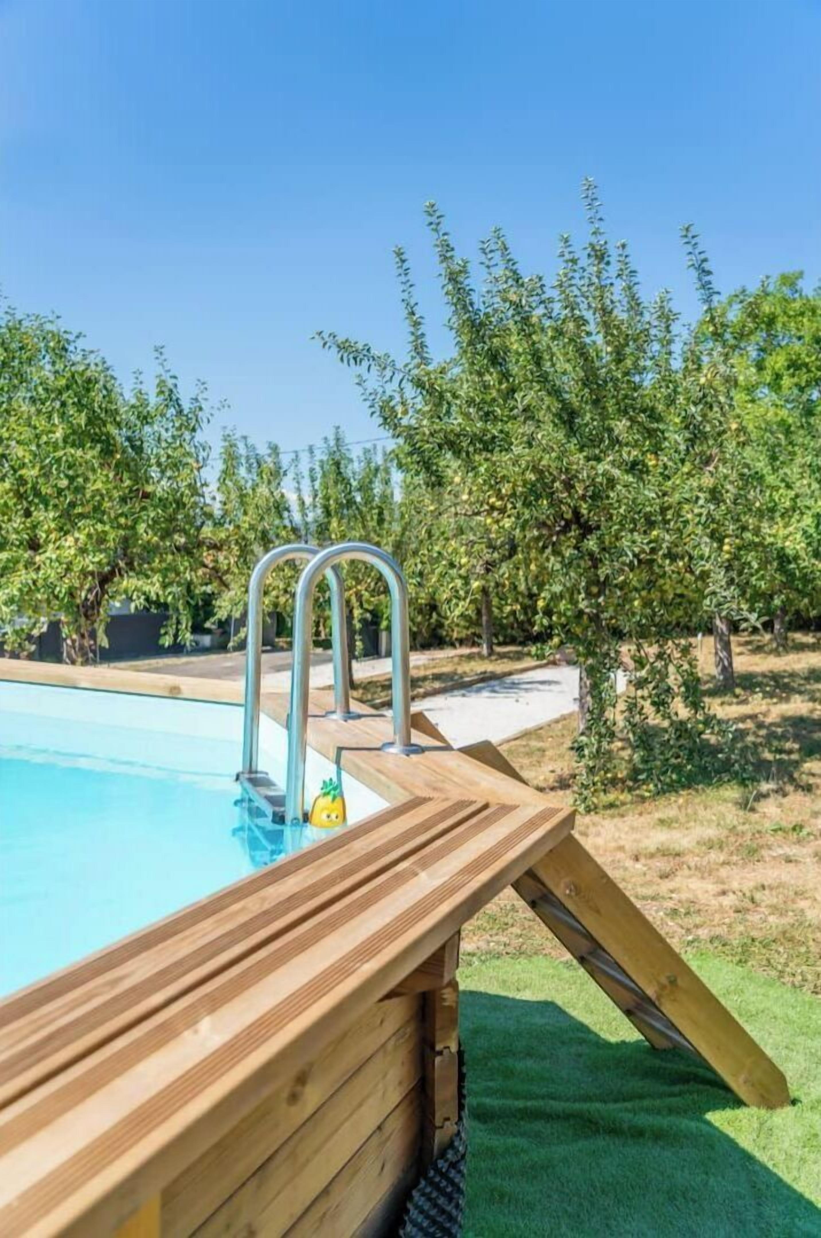 A swimming pool with a wooden deck and metal ladder, surrounded by trees and a grassy area.
