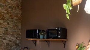 A kitchen with a stone wall, a wooden counter, a microwave, and a hanging plant. - Lexotique Cottage (Solliès-Pont)