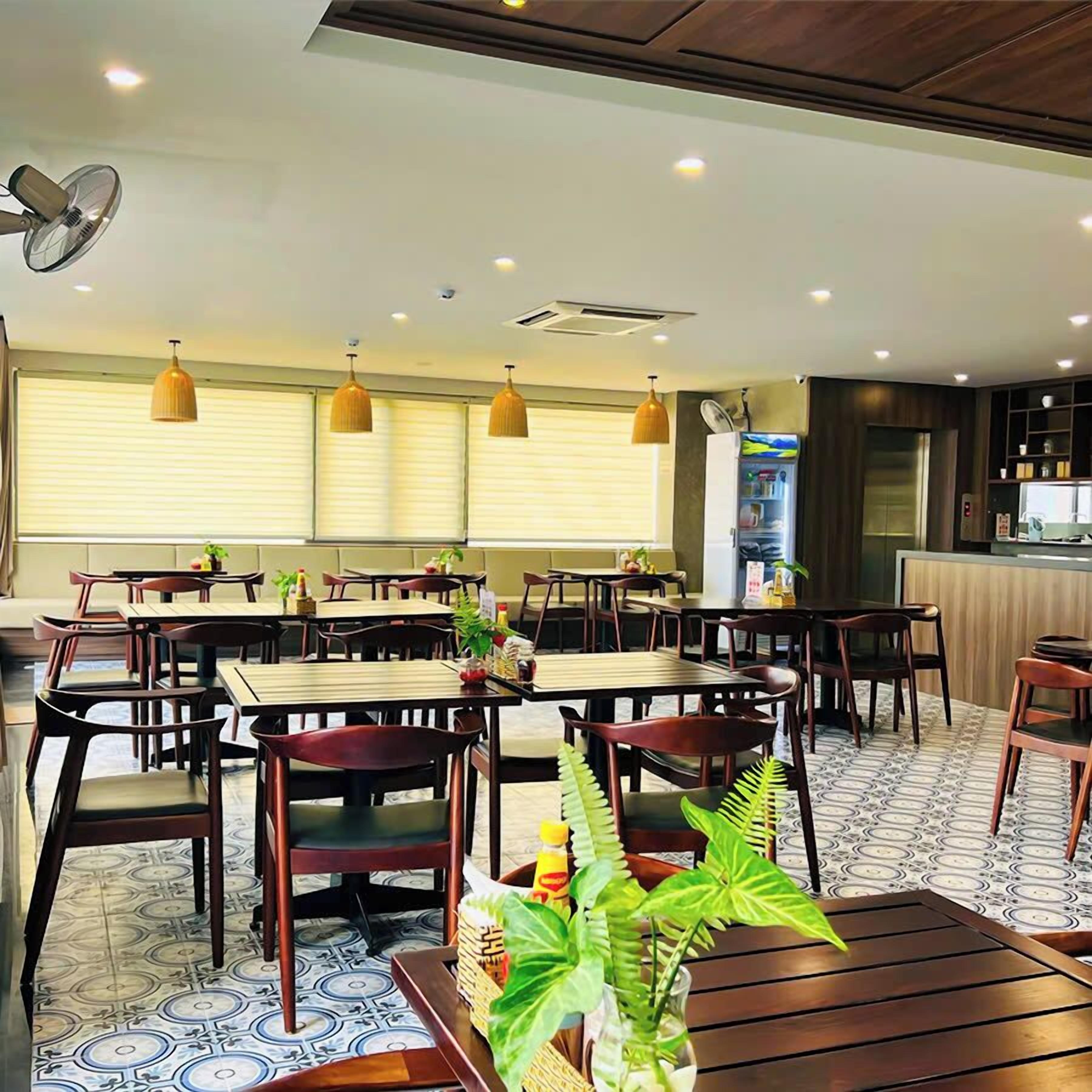 Een restaurant met meerdere tafels en stoelen, plafondventilatoren, hanglampen en een keuken in de achtergrond.