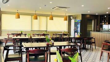 Een restaurant met meerdere tafels en stoelen, plafondventilatoren, hanglampen en een keuken in de achtergrond.