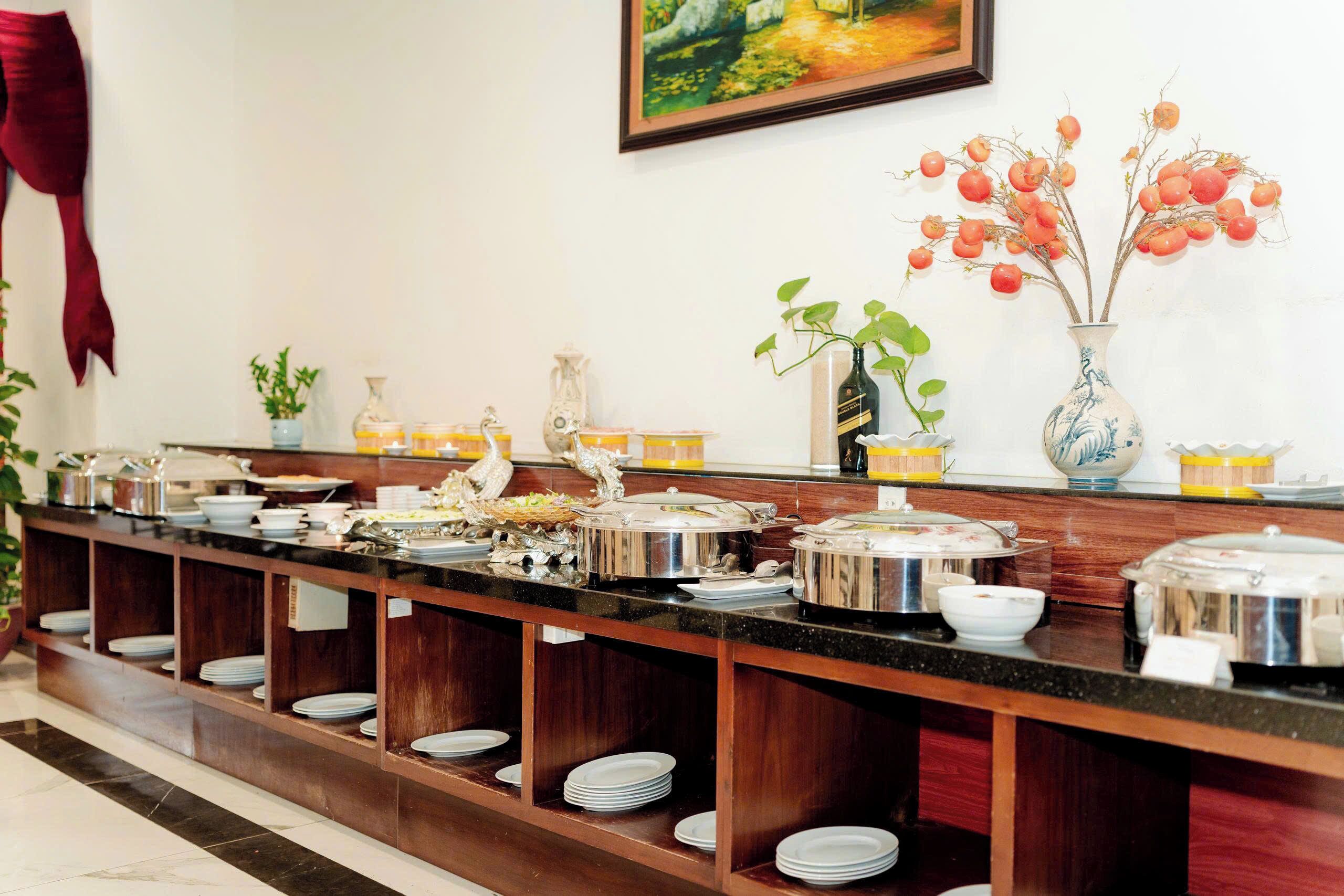 A buffet setup with various food containers and a decorative vase with red fruits on the counter.