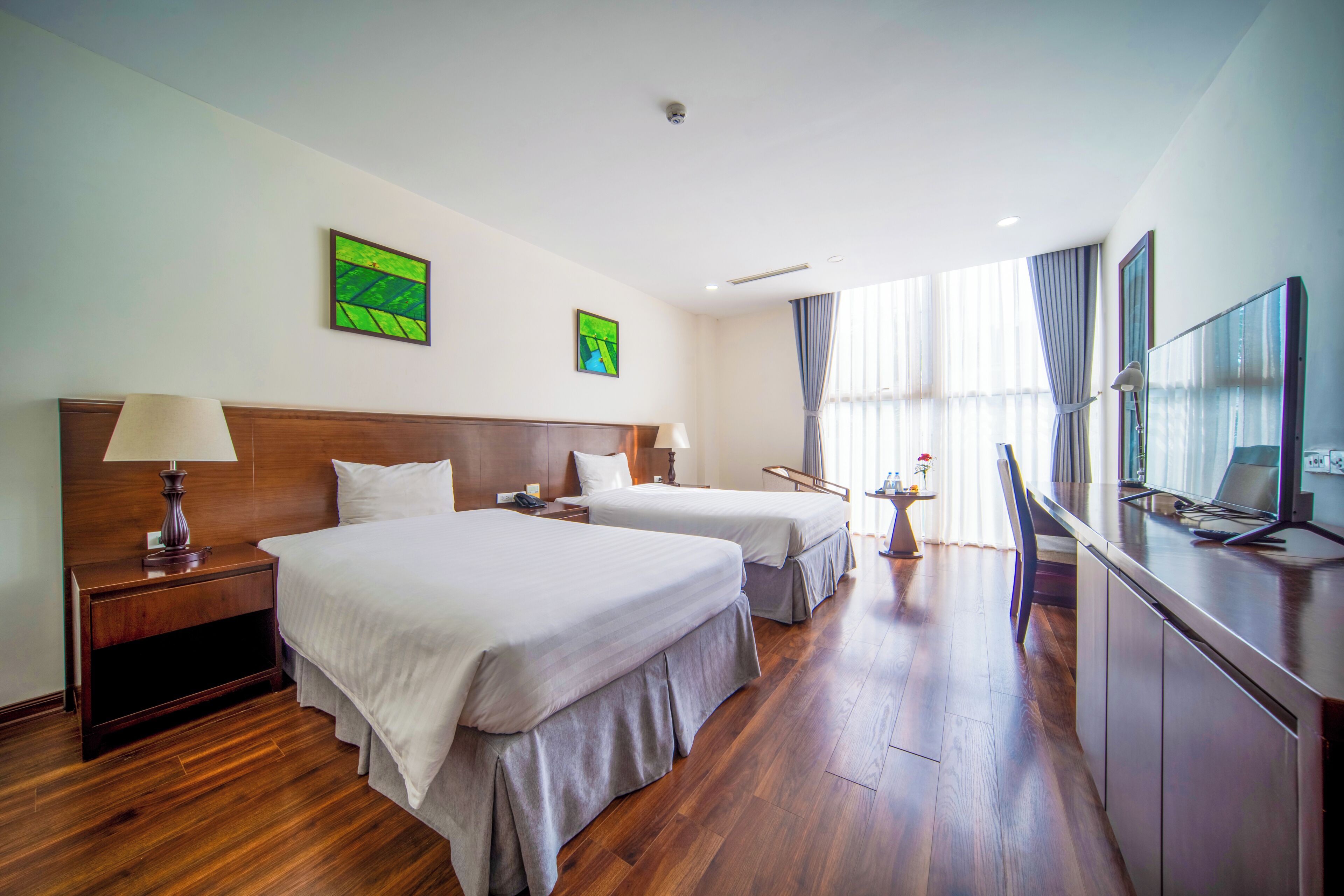 A hotel room with two beds, a desk with a computer, a TV, and a window with curtains.