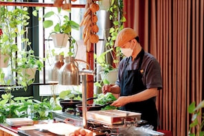 Una persona cocina en una cocina con plantas colgantes y un ventanal.