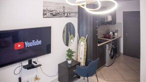 A modern living room with a flat-screen TV displaying the YouTube logo, a dining area with a kitchen, and a large mirror. - Beautiful Suite @Embassy Gardens (Accra)