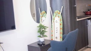A modern room with a flat-screen TV, a potted plant, a blue chair, and two decorative mirrors. - Beautiful Suite @Embassy Gardens (Accra)