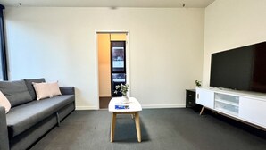 Un salon moderne avec un canapé gris, une table basse blanche, un téléviseur à écran plat posé sur un meuble blanc et une porte donnant sur un placard.
