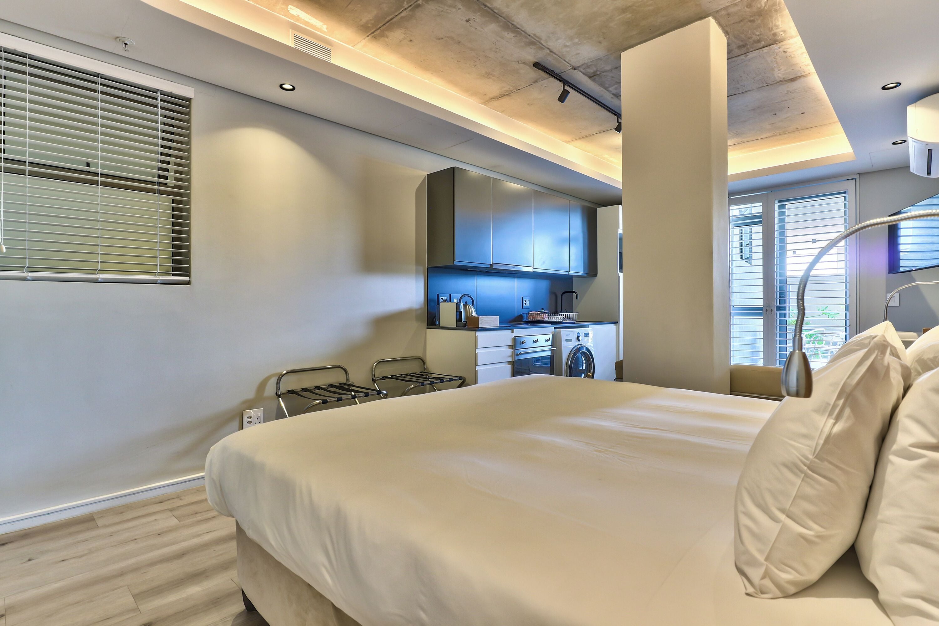 A modern bedroom with a large bed, a kitchenette, and a view of the outside.