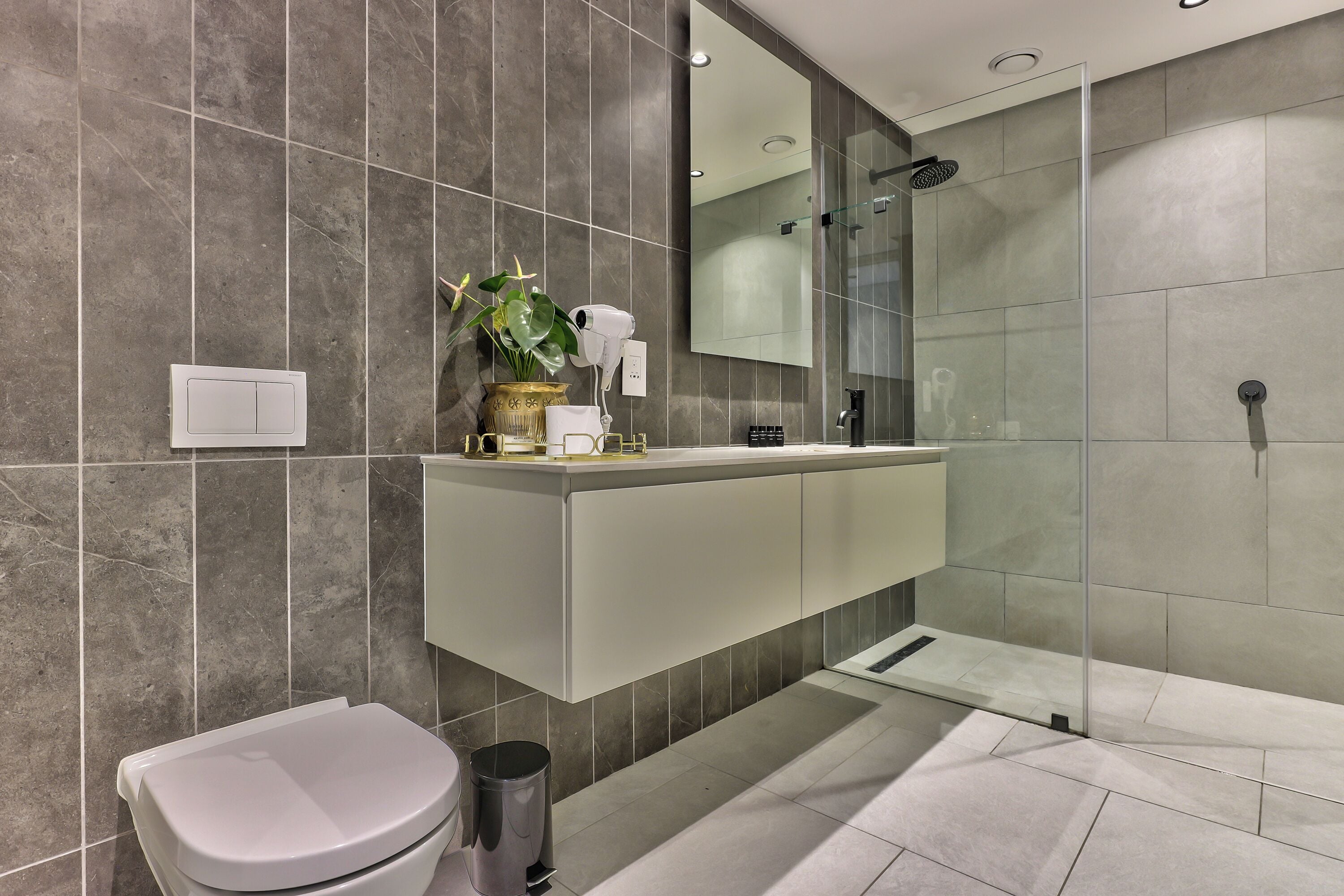 Un bagno moderno con box doccia in vetro, un mobile lavabo bianco e una pianta in vaso.