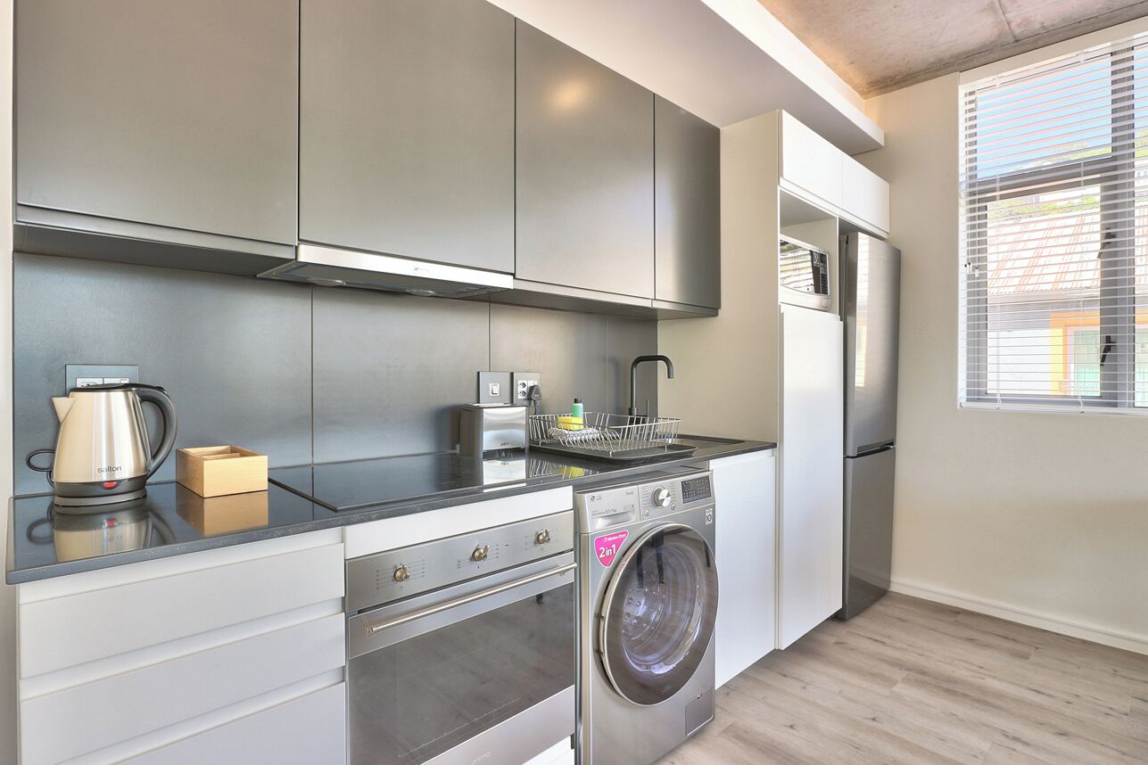 A compact kitchen with modern appliances, including a stainless steel oven, a built-in washing machine, and a refrigerator.