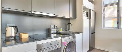 A compact kitchen with modern appliances, including a stainless steel oven, a built-in washing machine, and a refrigerator.