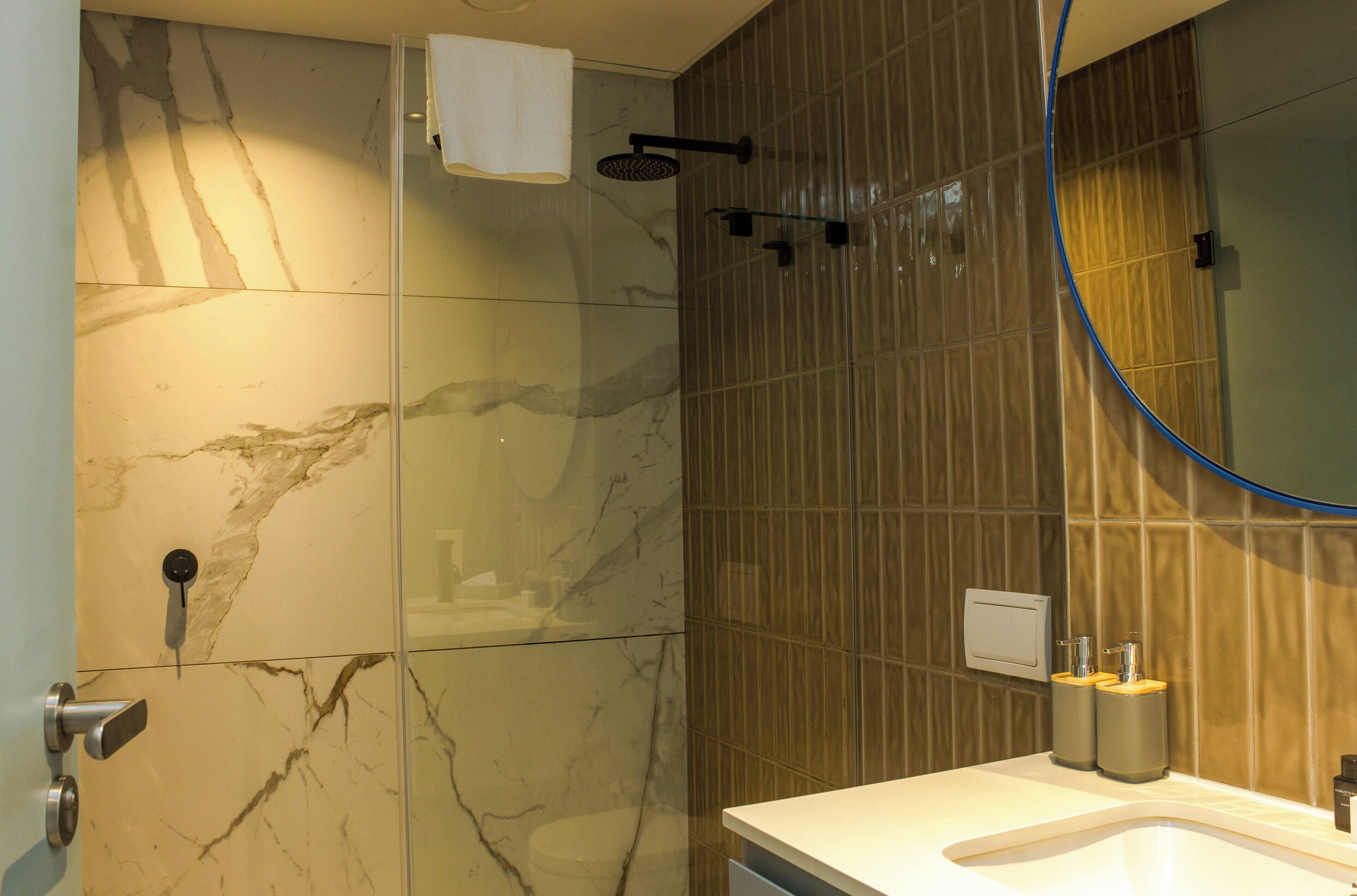 A bathroom with a marble shower wall, a glass door, a sink with a mirror, and a towel hanging on the wall.