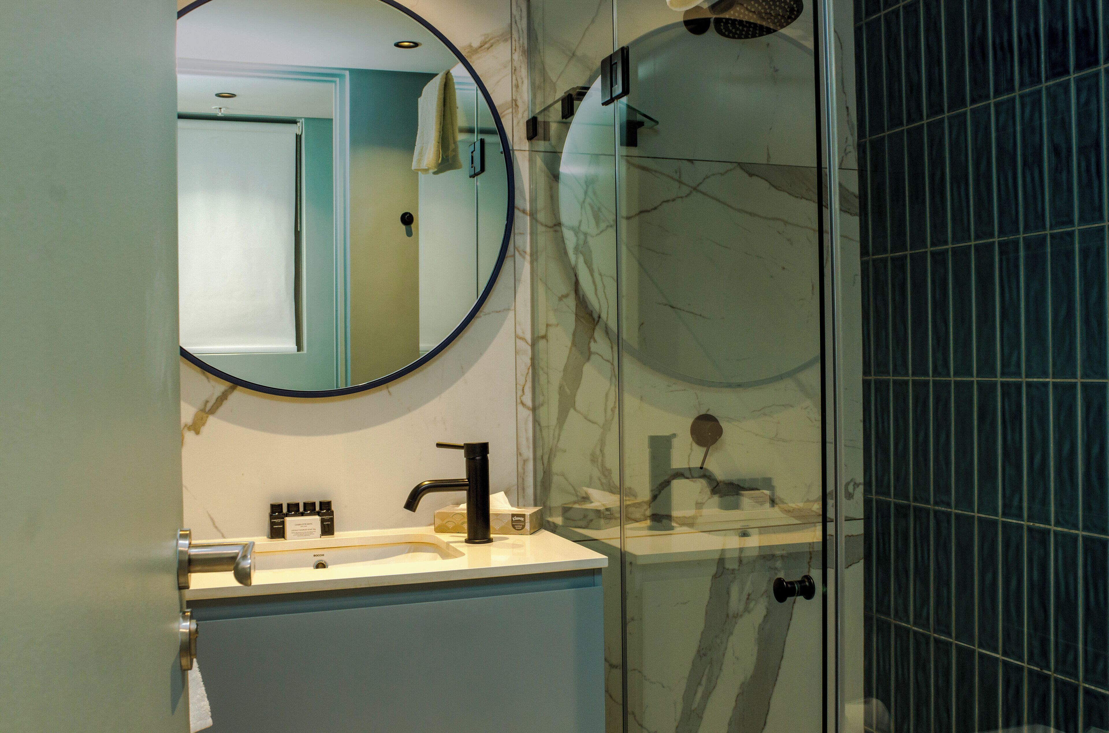 Ein Badezimmer mit Marmorwaschbecken, einem runden Spiegel und einer Duschkabine aus Glas.